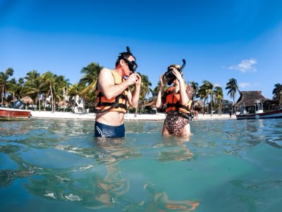 Family in life jackets snorkelling together in the shallows at Akumal