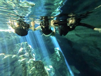 Underground cenote lit from above, stalactites over deep blue water
