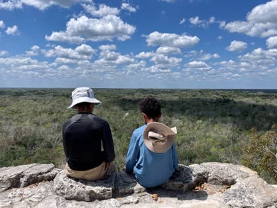 Two kids sitting on the Coba pyramid, looking out over the jungle